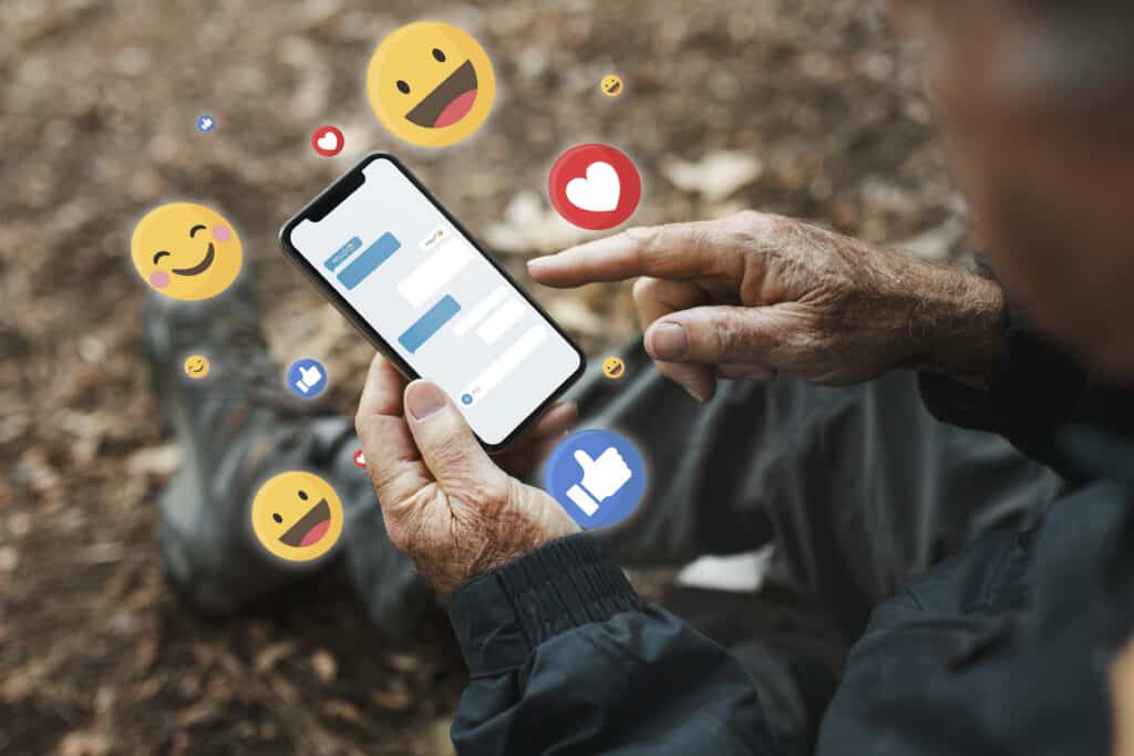 Person using a smartphone with chat bubbles and social media emojis floating above the screen outdoors. | Tsunami Reach