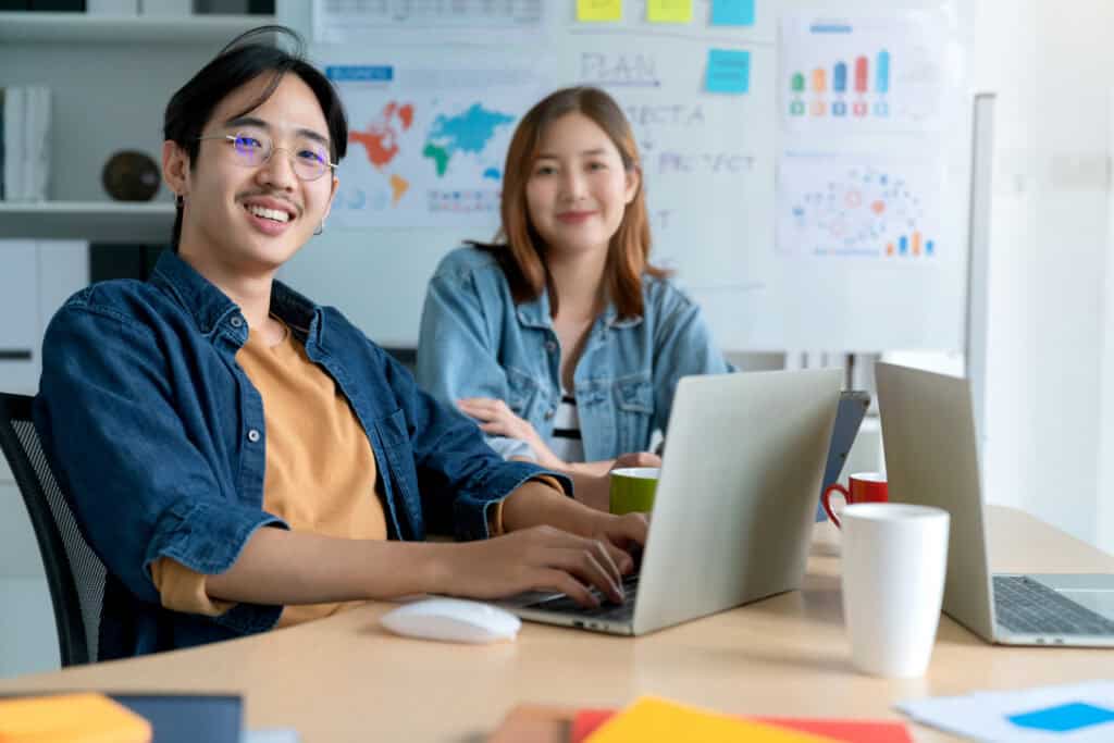 Two Asian office workers smiling while working on content marketing in a bright, modern creative workspace. | Tsunami Reach
