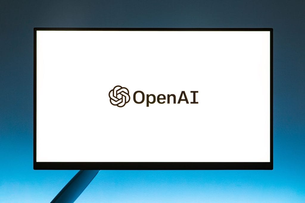 A monitor displays the OpenAI logo and name on a white background with a blue gradient backdrop. | Tsunami Reach