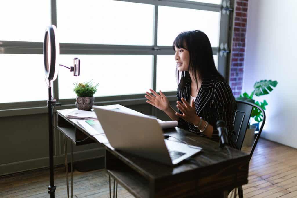 Woman speaking in front of a smartphone and laptop at a desk, recording a video in a modern office space. | Tsunami Reach
