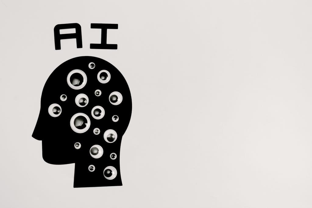 Black silhouette head with multiple googly eyes and “AI” text above, on a white background. | Tsunami Reach