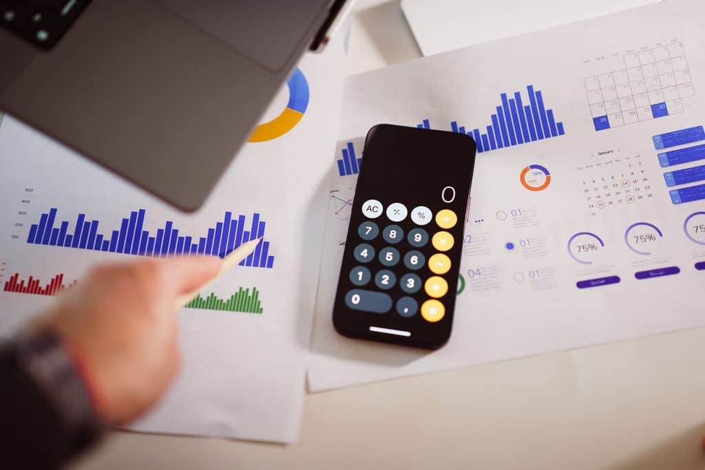 A smartphone calculator on papers with charts, graphs, and a hand pointing at data with a pen. | Tsunami Reach