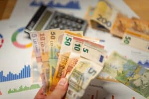 Hand holding Romanian banknotes over charts, with a calculator and more cash in the background on a desk. | Tsunami Reach