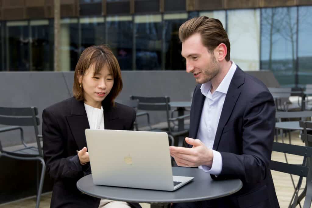 A woman and a man in business attire sitting at a table outdoors and looking at a laptop. | Tsunami Reach