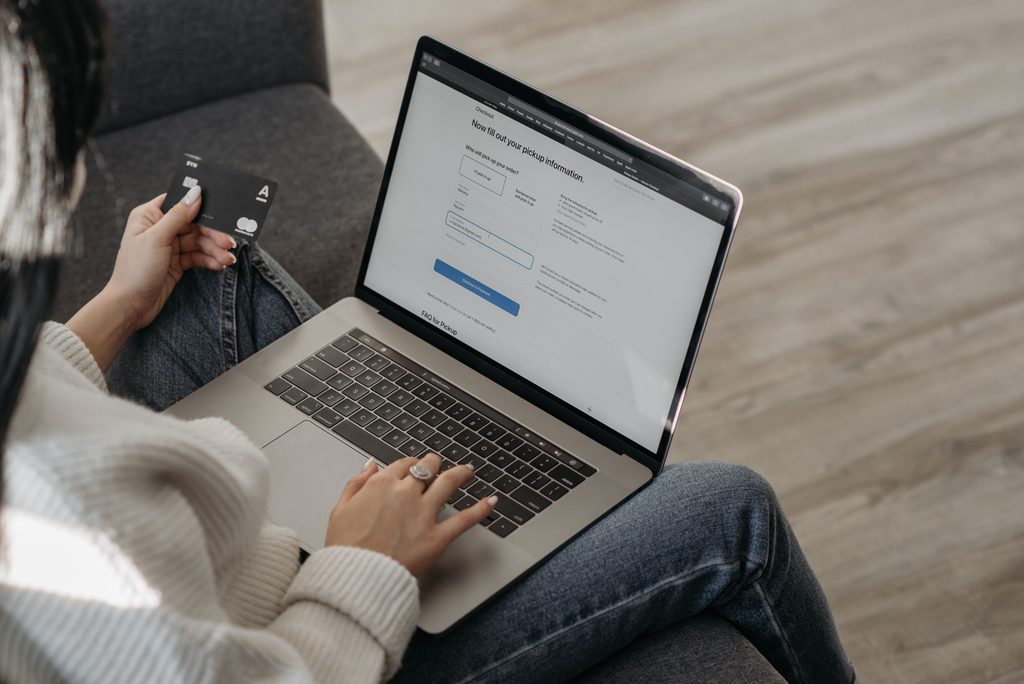 Person holding a credit card and using a laptop to fill out an online payment form while sitting on a couch. | Tsunami Reach