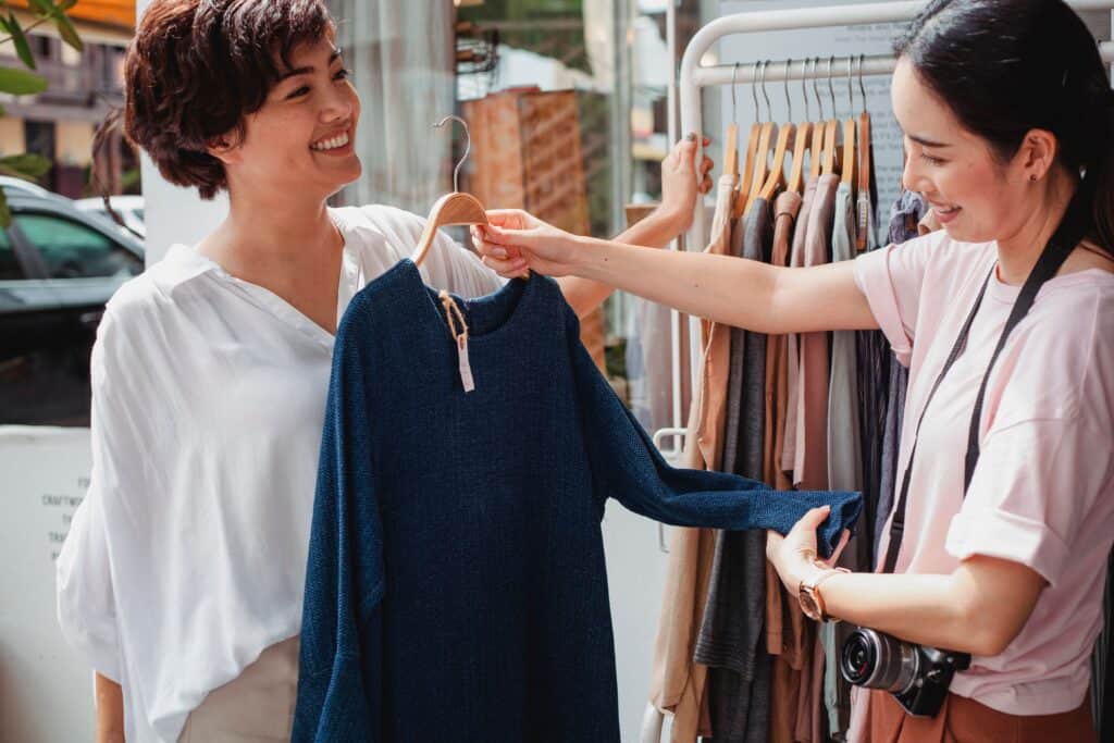 A woman shows a blue long-sleeved shirt to a customer, highlighting e-commerce growth in a clothing store. | Tsunami Reach